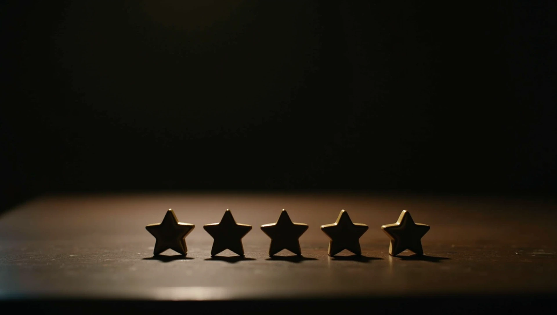 Five small brass stars in a row on a dark wooden desk, lit by a single lamp.